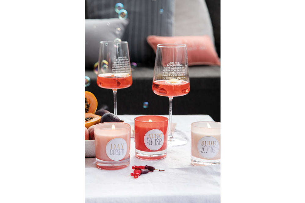 Duftkerze Daydream, Atempause und Ruhezone in verschiedenen Rottönen mit Weingläsern auf einem Tisch mit Seifenblasen im Hintergrund