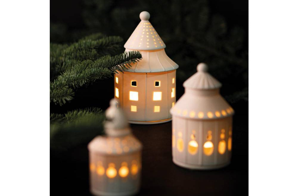 Räder - Lichthaus "Traumhaus" weißes rundes Lichthaus aus Porzellan mit verschieden großen löchern, beleuchtet mit anderen Lichthäusern auf dem Couchtisch dekoriert mit Tannenzweigen Nahaufnahme
