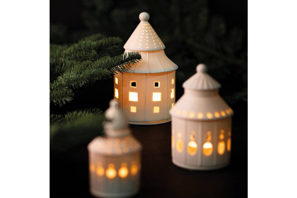 Räder - Lichthaus "Traumhaus" weißes rundes Lichthaus aus Porzellan mit verschieden großen löchern, beleuchtet mit anderen Lichthäusern auf dem Couchtisch dekoriert mit Tannenzweigen Nahaufnahme